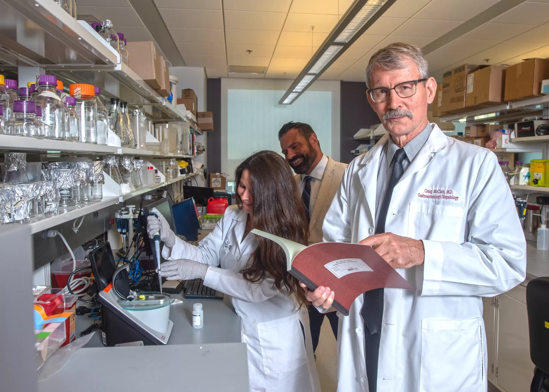 Dr. McClain looks toward the camera with two other researchers in the background of a lab environment